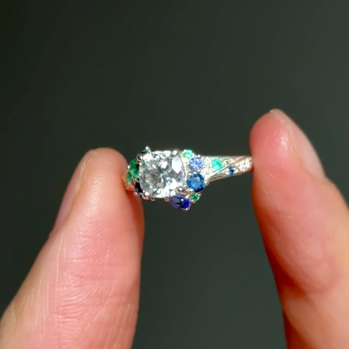 Diamond ring held between two fingers against a dark background