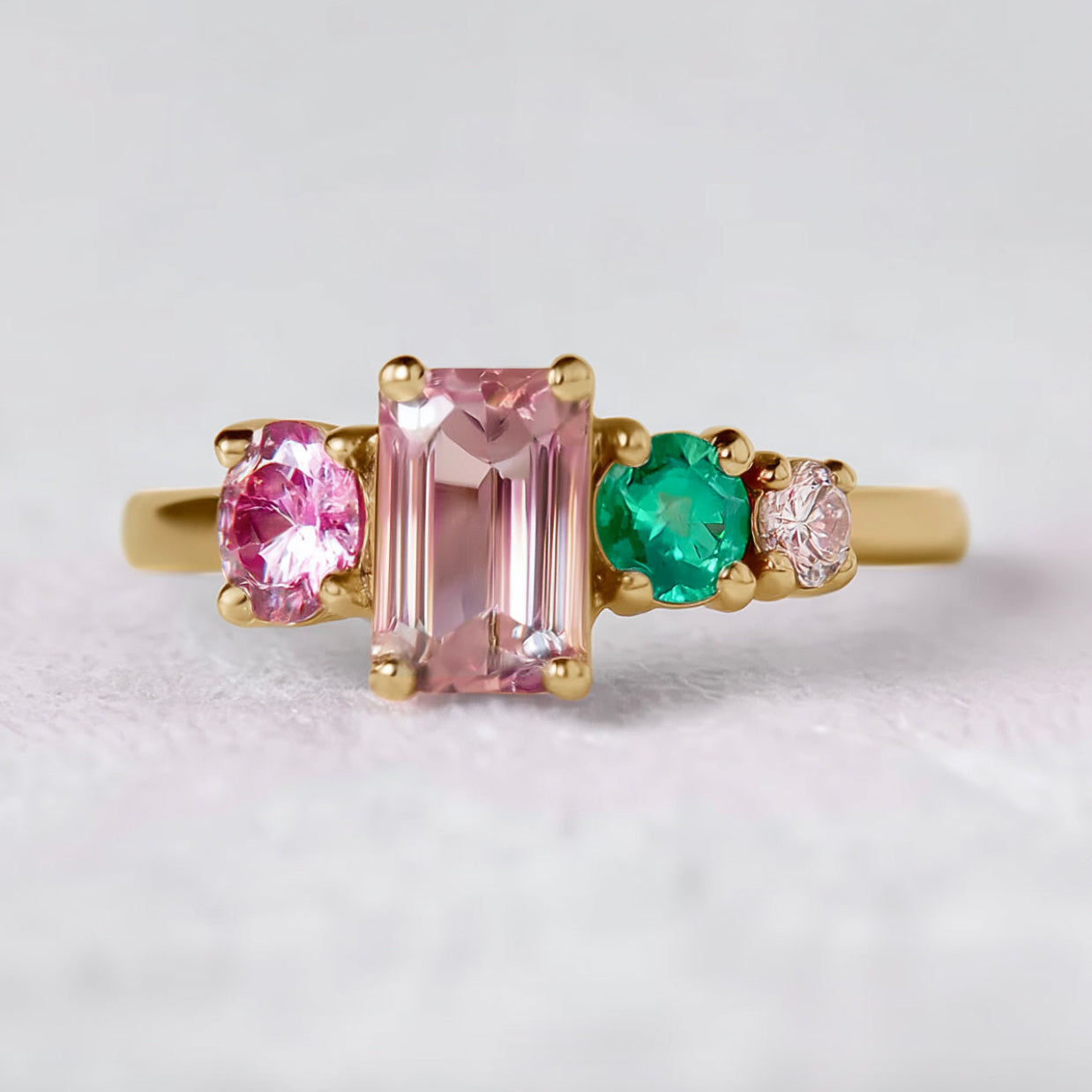 Gold ring with pink and green gemstones on a light gray background