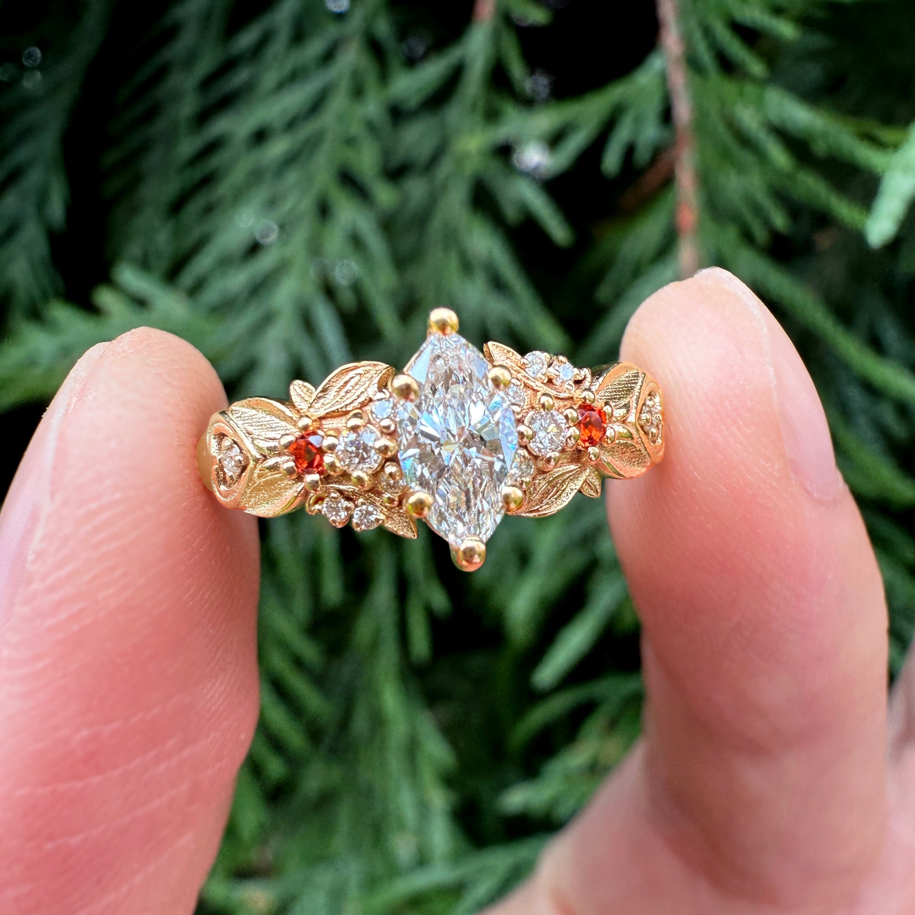 Gold ring with a large diamond held between two fingers against a green leafy background