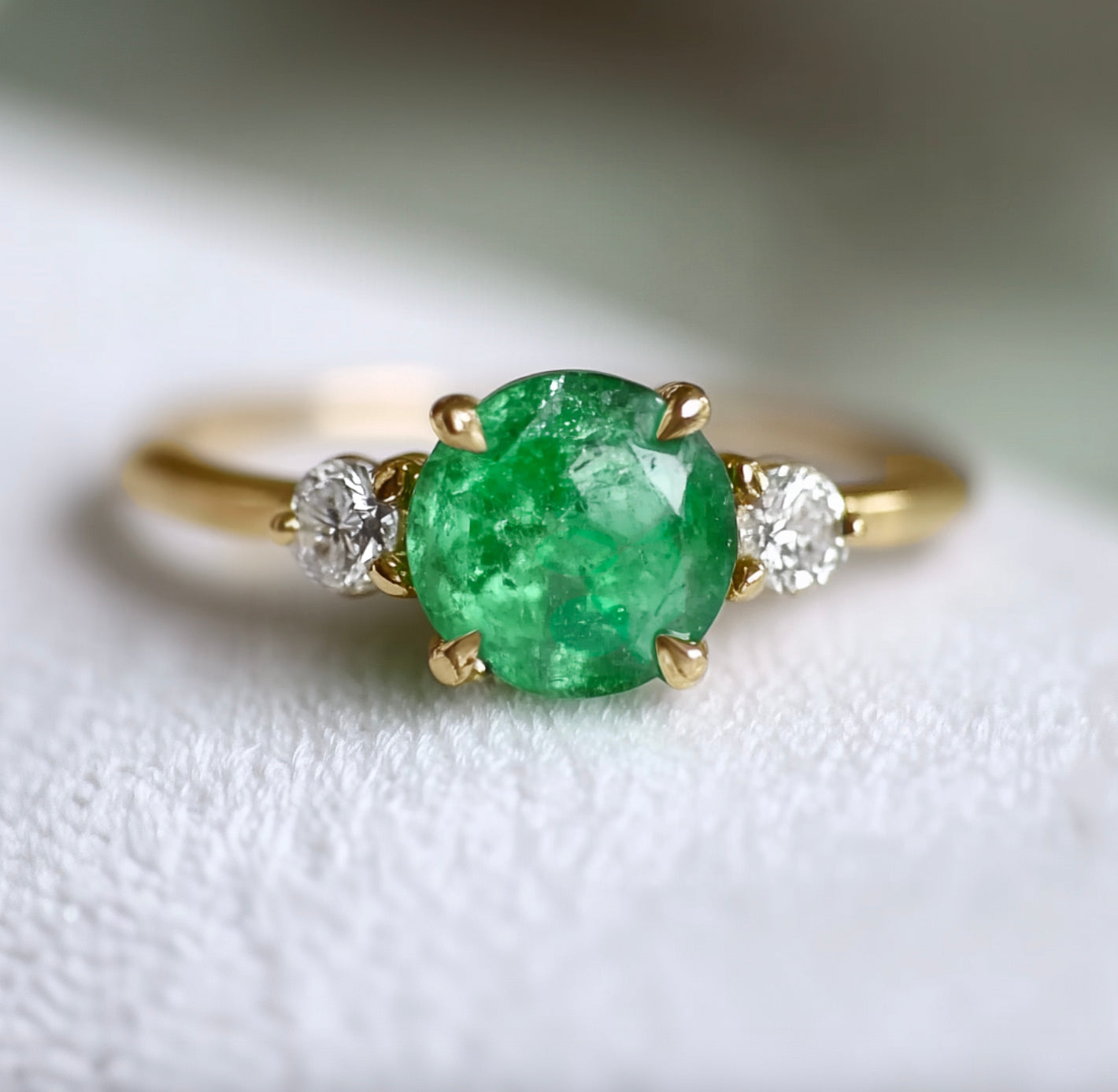 Gold ring with a green gemstone and two smaller diamonds on a light background