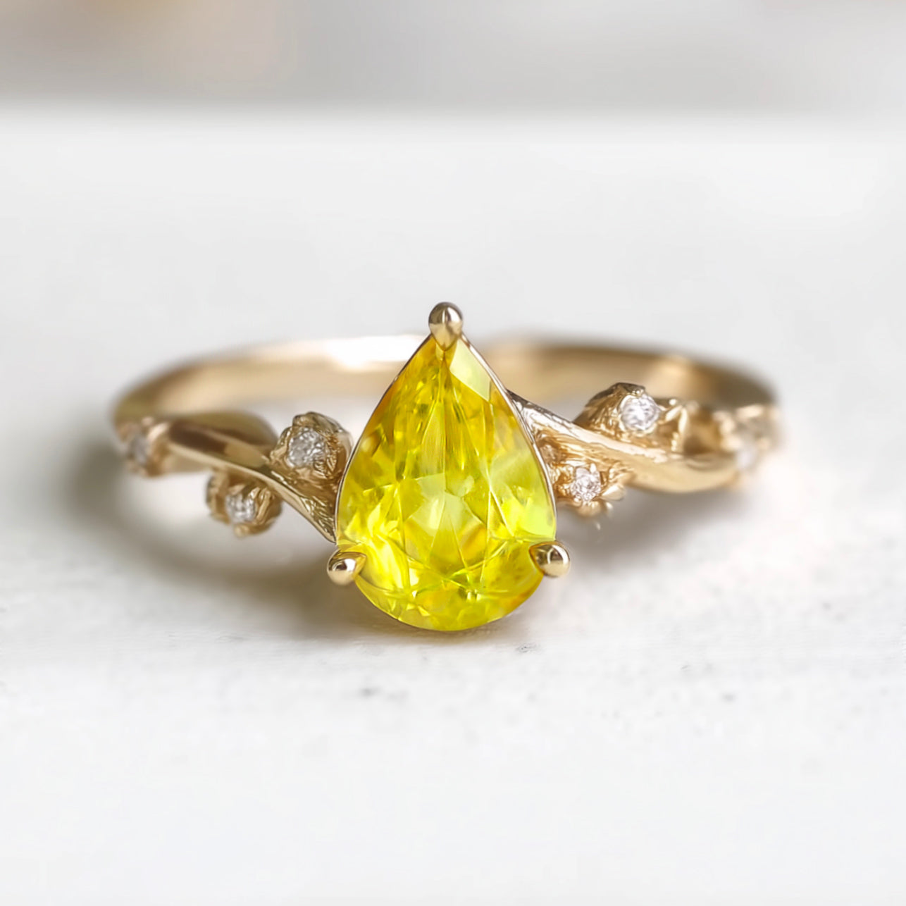 Gold ring with a yellow pear-shaped gemstone on a light background