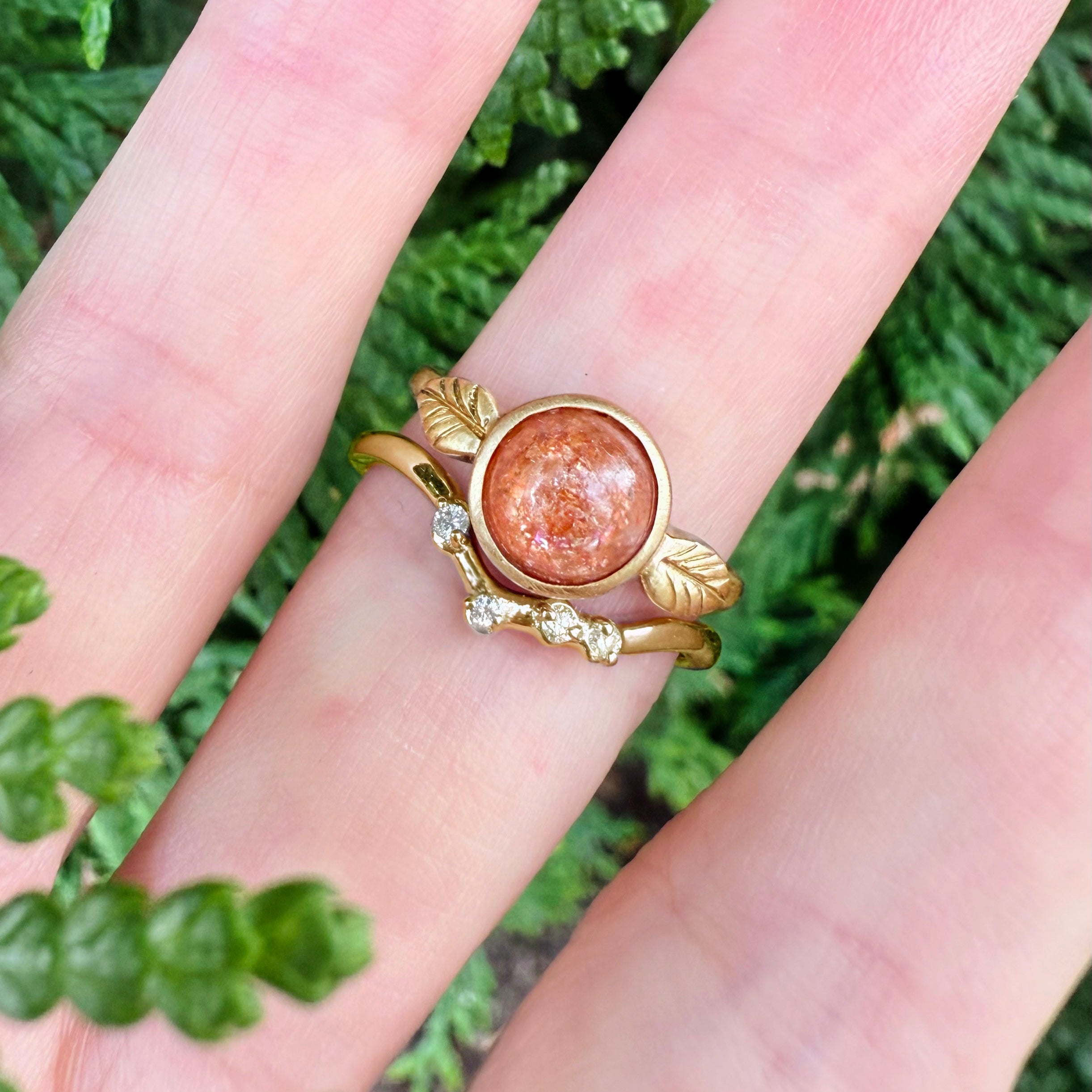 Gold ring with a sunstone on a hand against a green leafy background