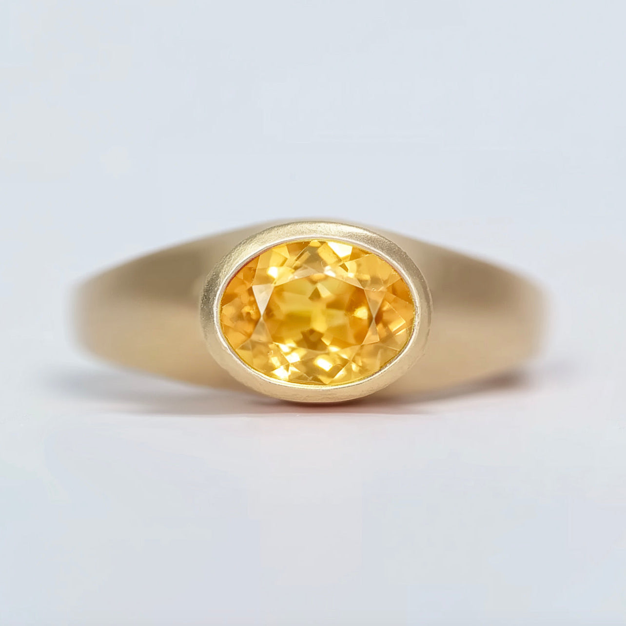 Gold signet ring with a yellow gemstone on a light gray background