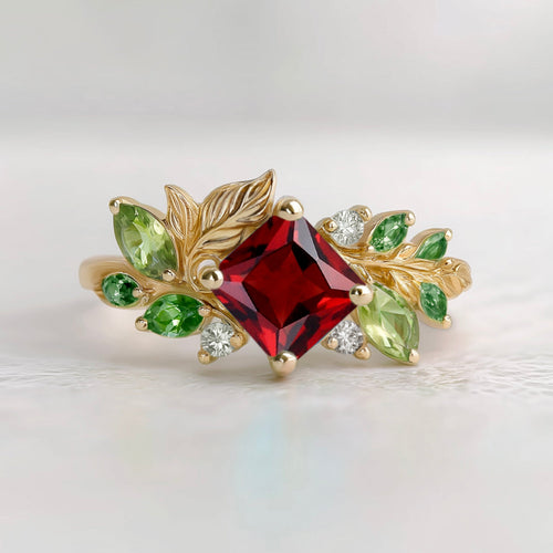 Gold ring with a red gemstone and green leaves on a light background