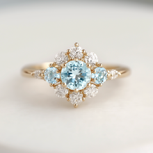 Load image into Gallery viewer, Elegant ring with a central blue gemstone and smaller diamonds on a light background
