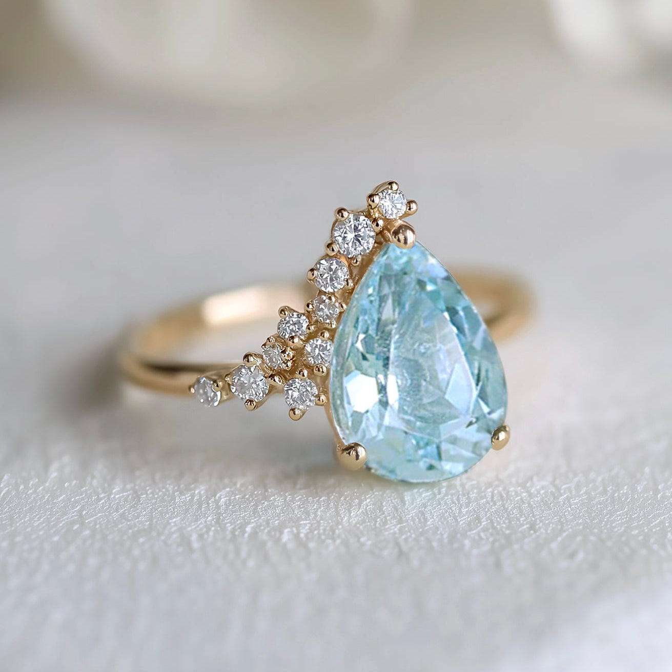 Gold ring with a large teardrop-shaped blue gemstone and smaller diamonds on a light background