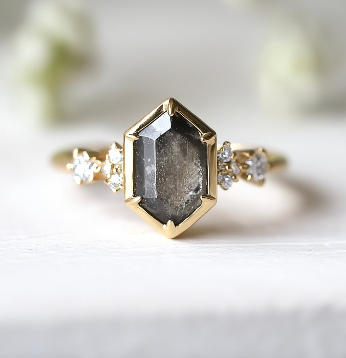 Gold ring with a hexagonal dark stone and smaller diamonds on a white background