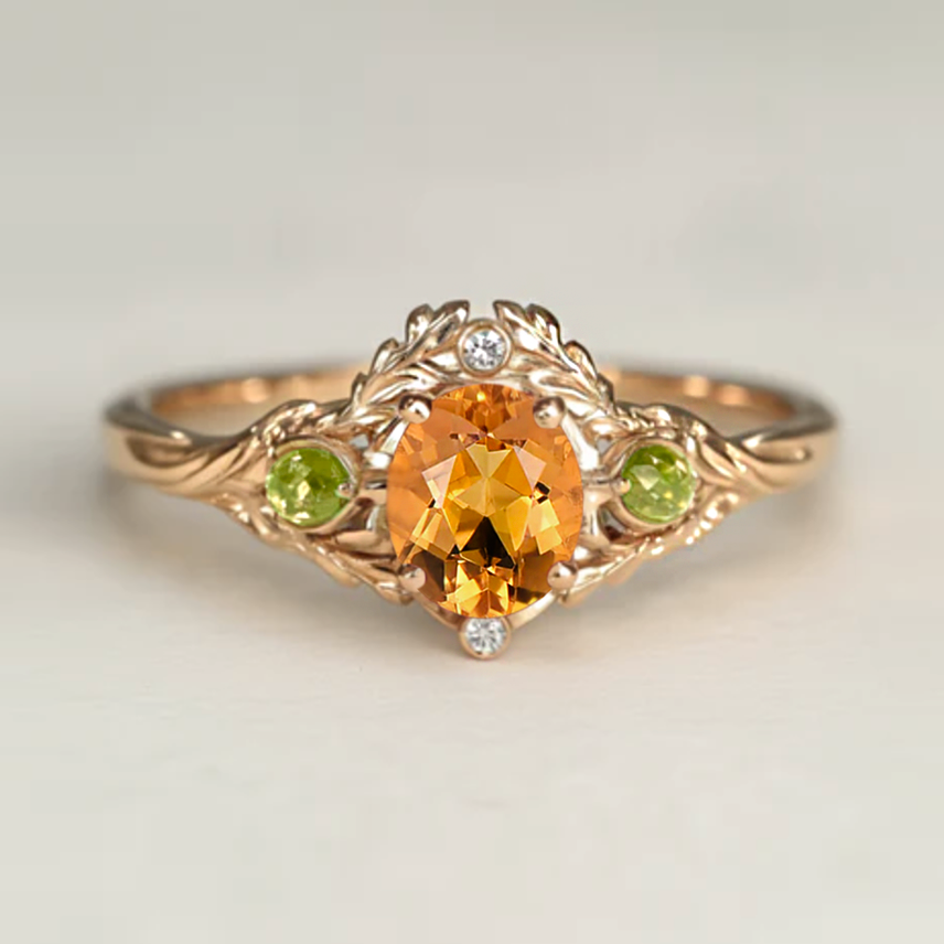 Gold ring with a central orange gemstone, flanked by green and white gemstones on a light gray background