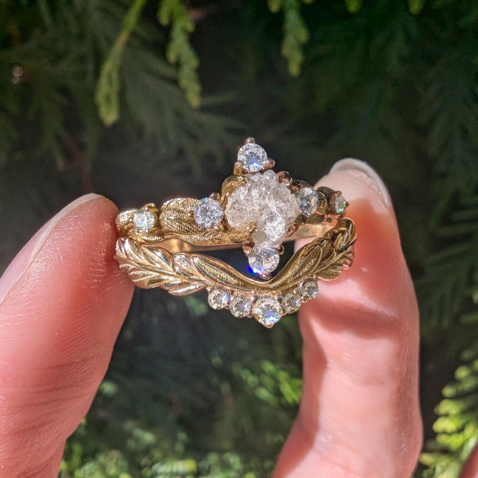 Gold ring with diamond details held between fingers against a green leafy background