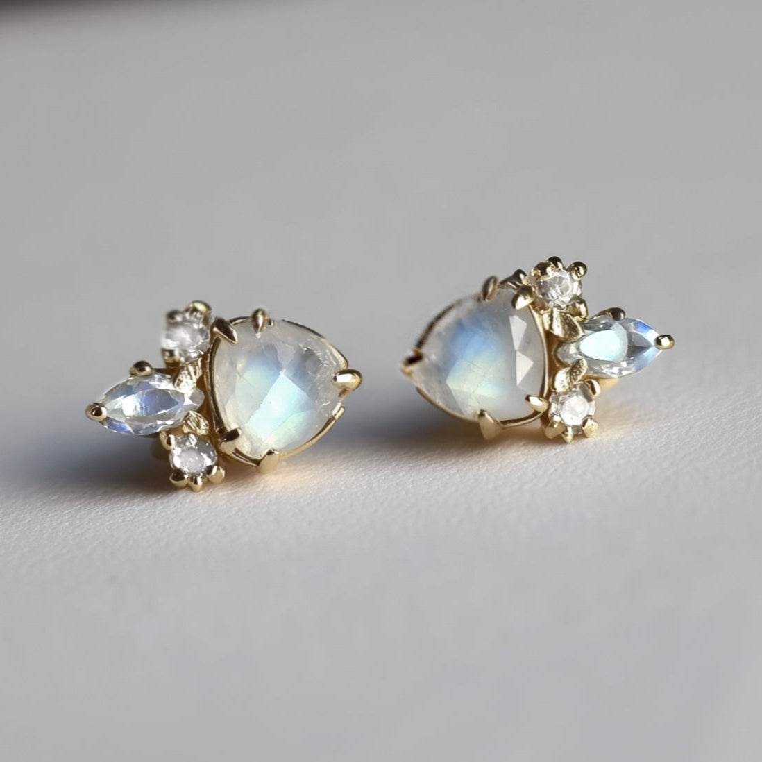 Pair of gold earrings with moonstone stones on a light gray background