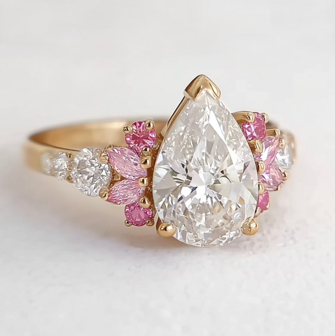 Gold ring with a large pear-shaped diamond and smaller pink and white diamonds on a light background