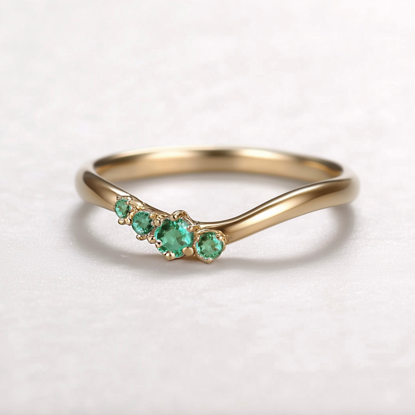Gold ring with emerald stones on a light gray background