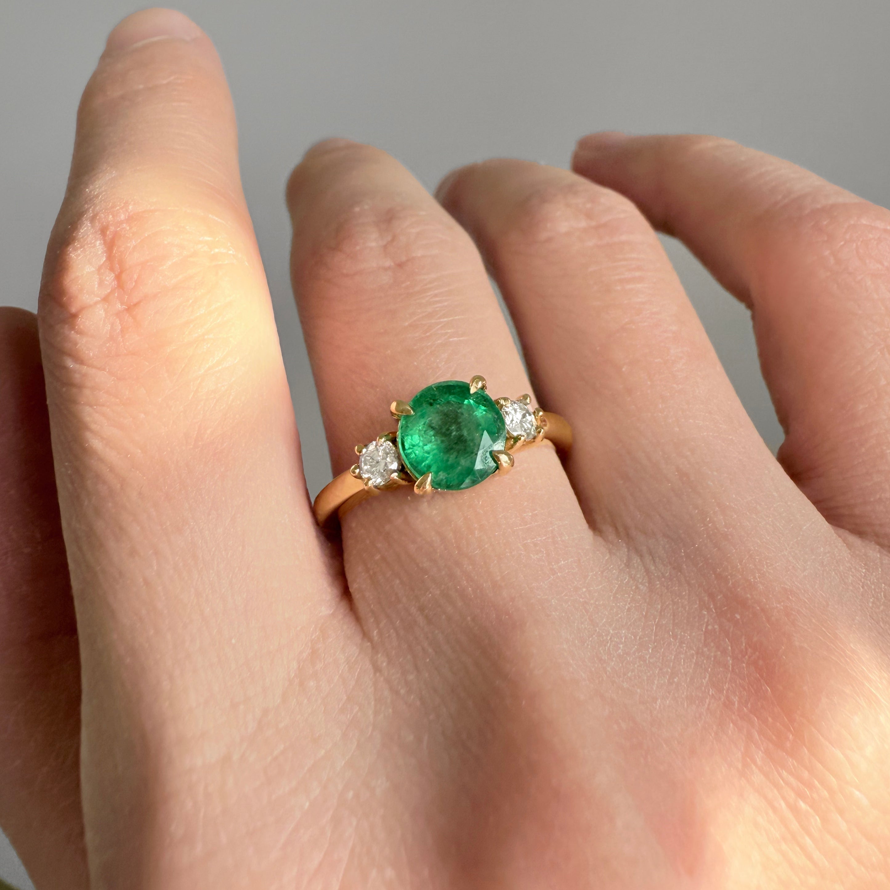 Gold ring with a green emerald on a person's finger against a neutral background