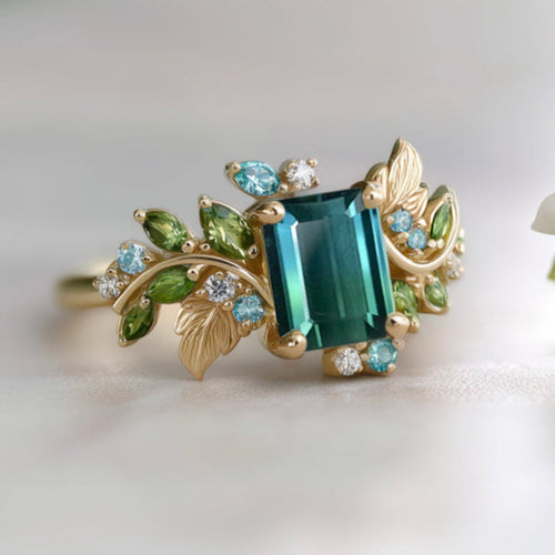 Gold ring with blue green rectangle gemstone and leaf designs on a light background