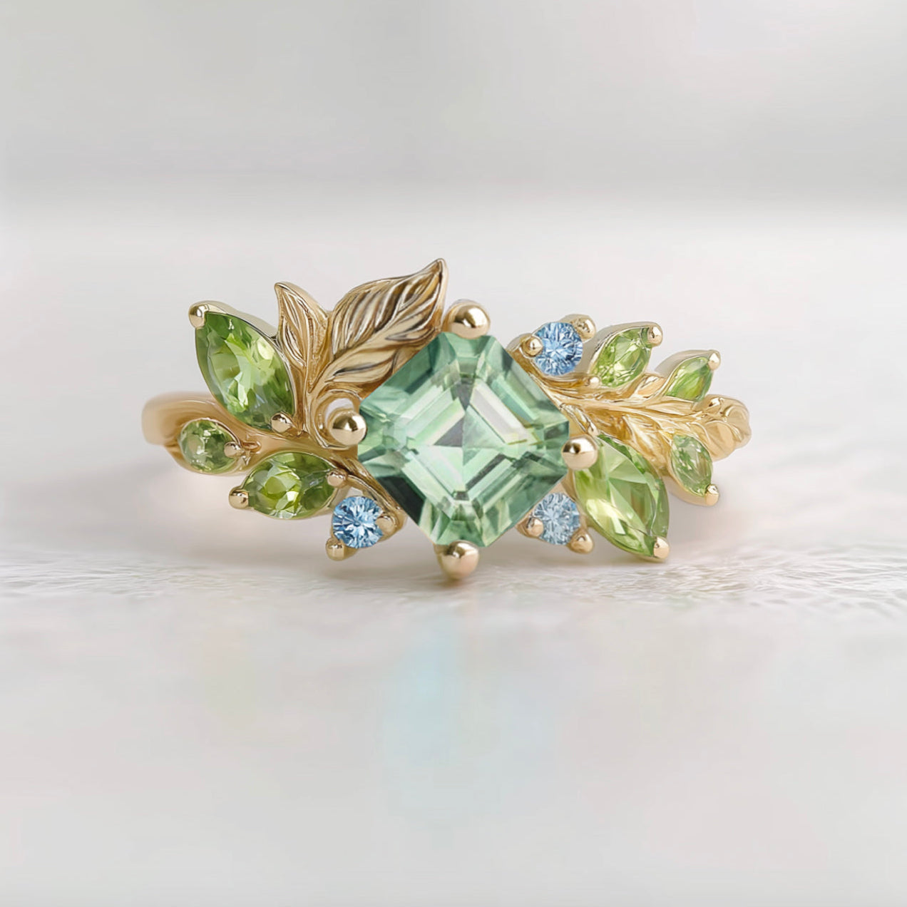 Gold ring with green gemstones and leaves on a light background