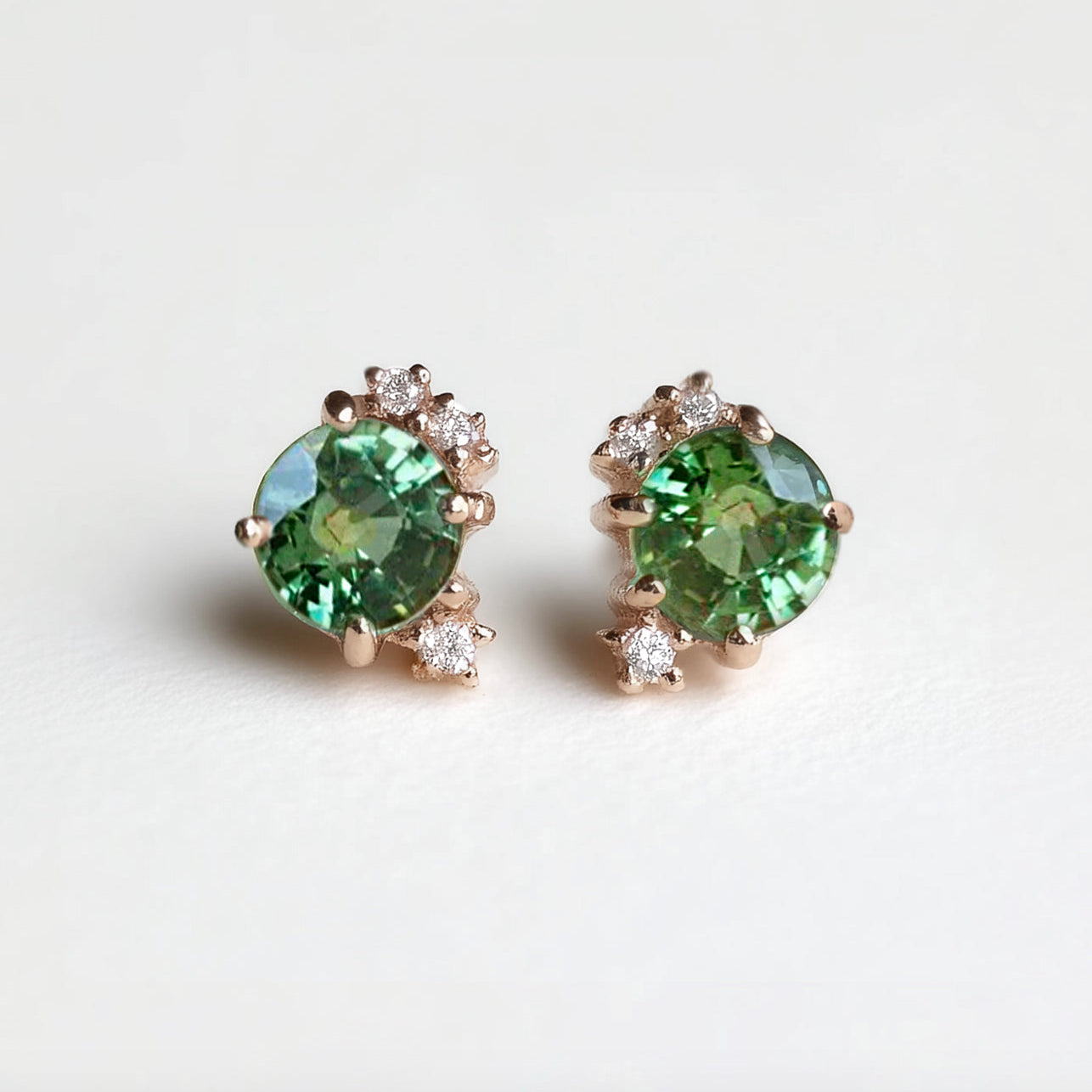 Pair of green blue sapphire earrings with rose gold setting on a white background