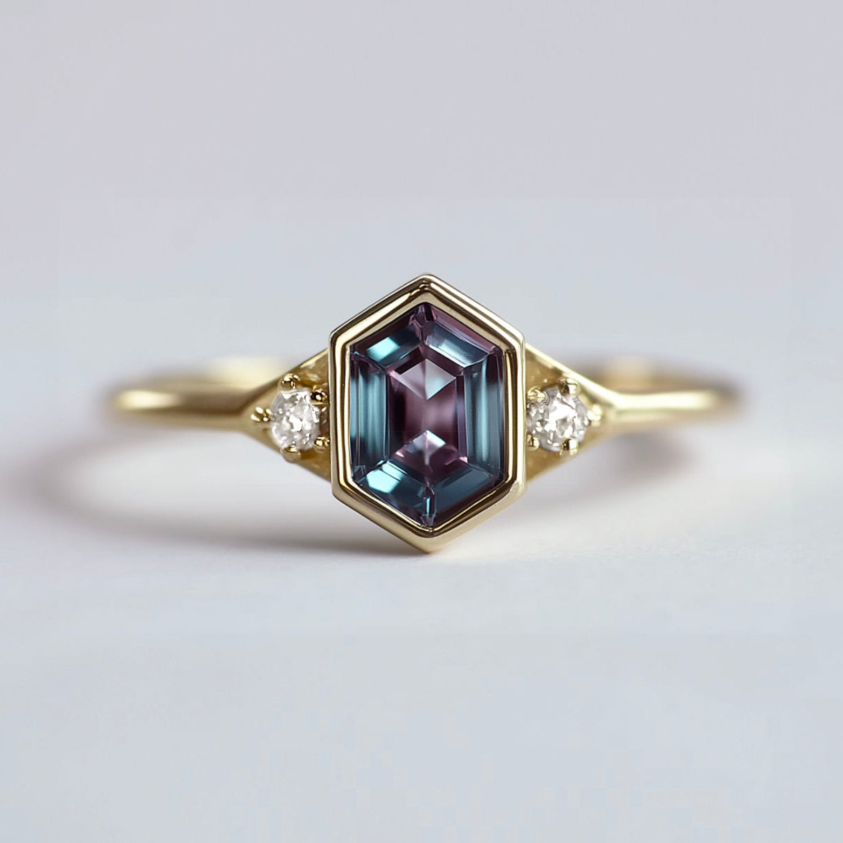 Gold ring with a hexagon gemstone and smaller diamonds on a light gray background