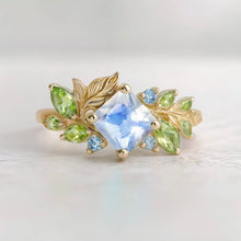 Load image into Gallery viewer, Gold ring with a central blue moonstone and green peridot accent stones 
