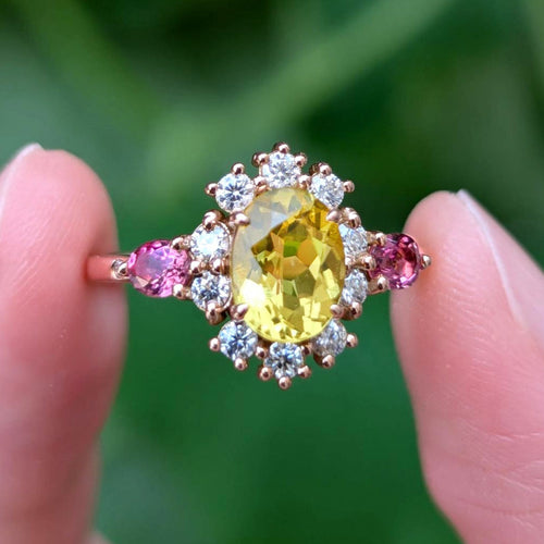 Ring with a yellow gemstone held between two fingers against a blurred green background