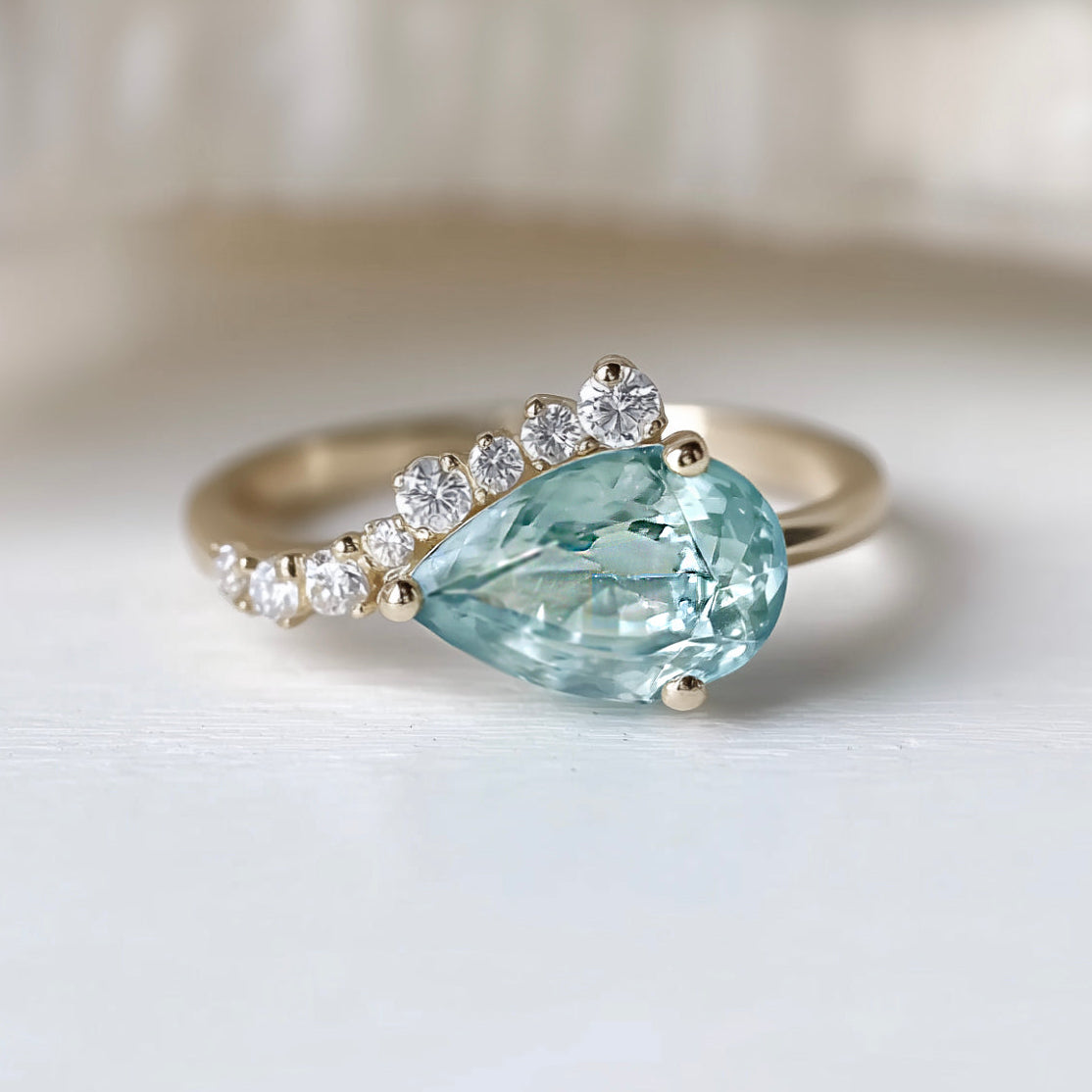 Ring with a pear-shaped green gemstone and diamond accents on a light background