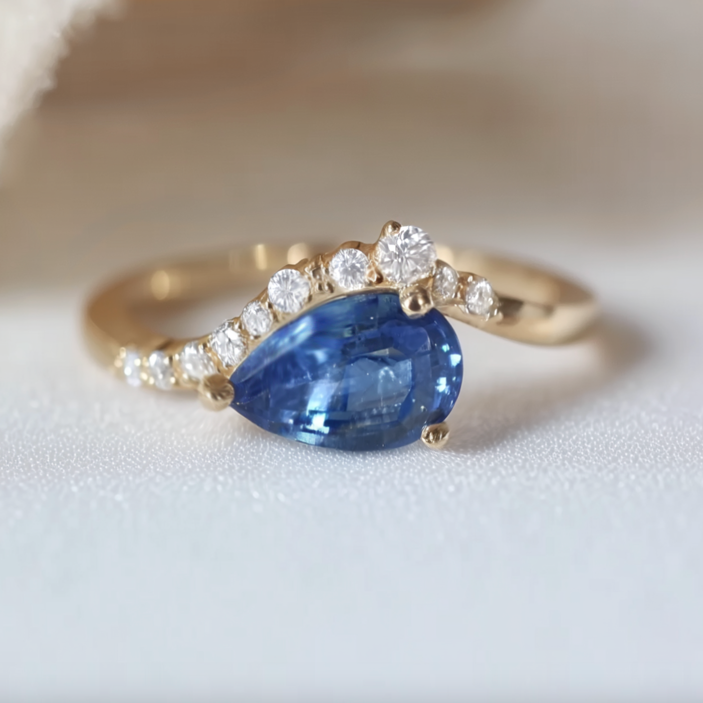 Gold ring with a blue sapphire gemstone and diamonds on a light background