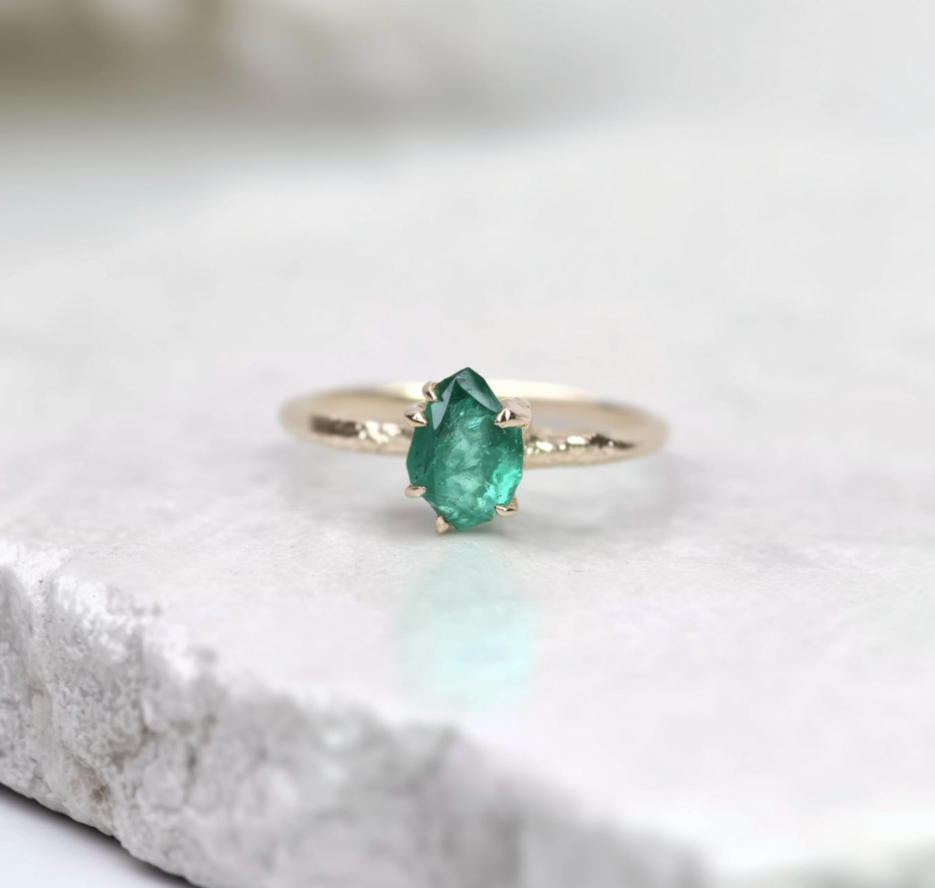 Gold ring with a green gemstone on a textured white surface