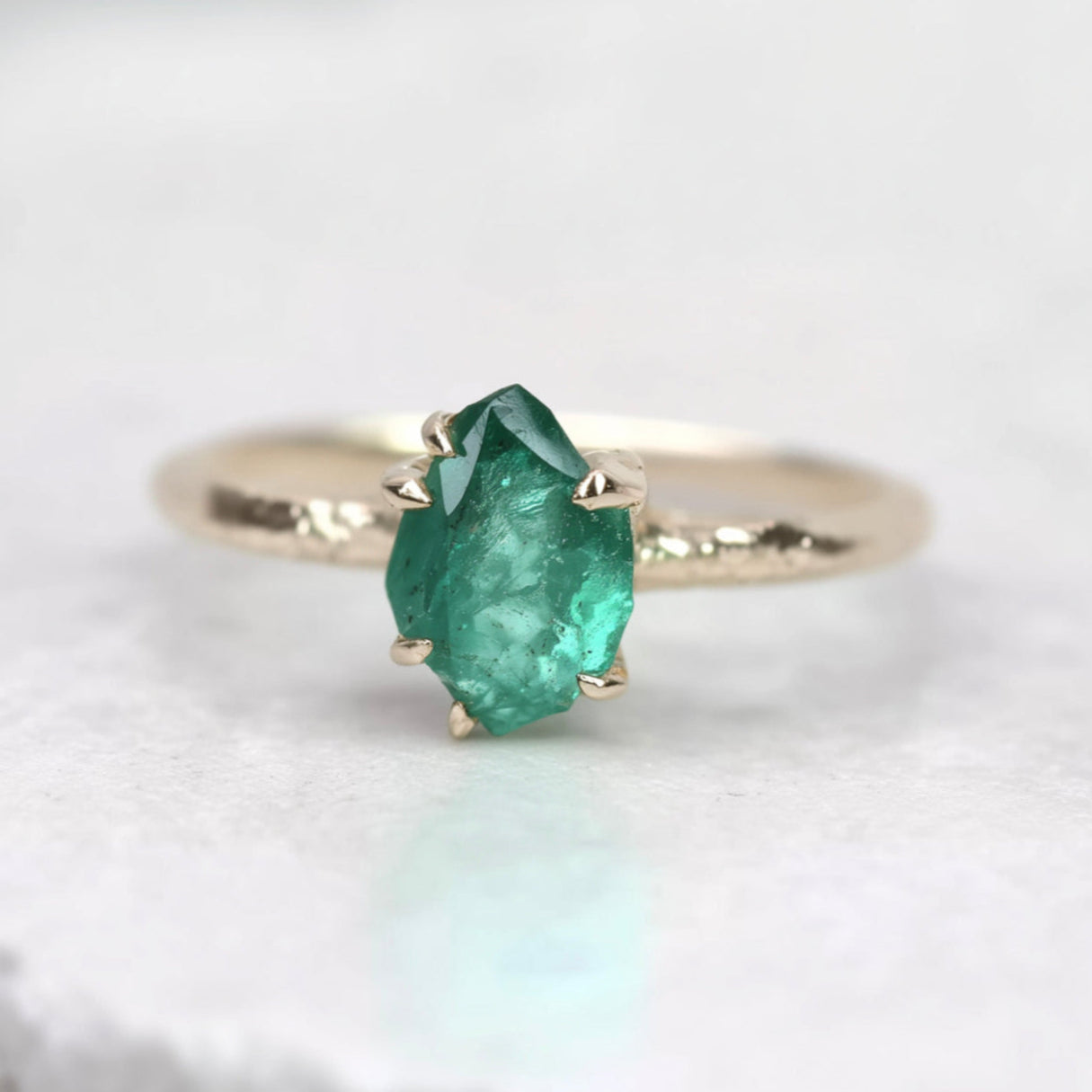 Gold ring with a green emerald stone on a light background