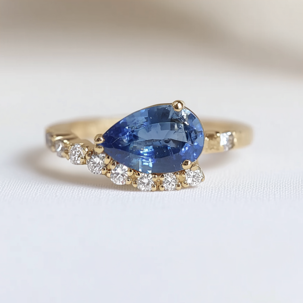 Gold ring with a blue pear-shaped gemstone and smaller diamonds on a white background