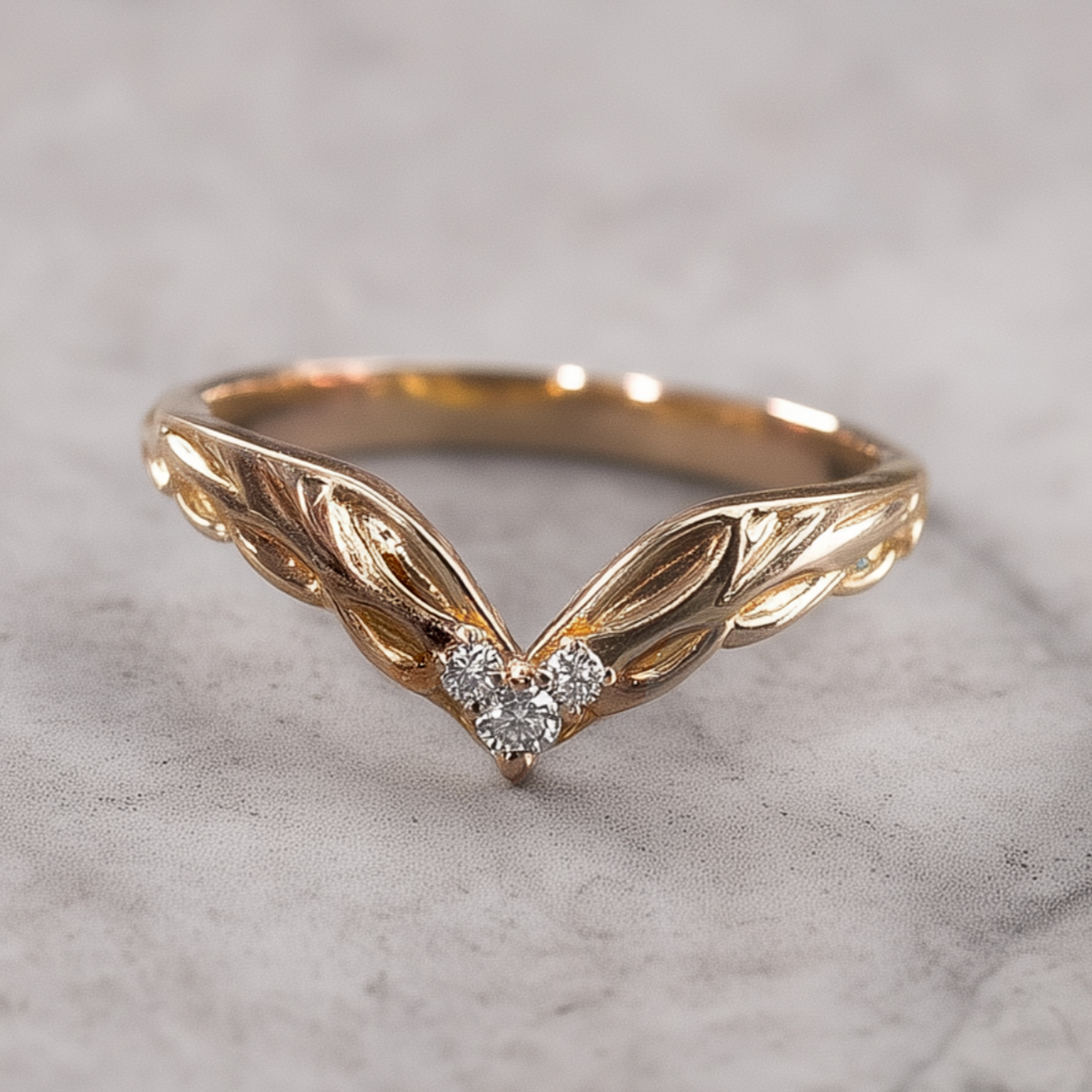 Gold ring with leaf design and two diamonds on a marble surface