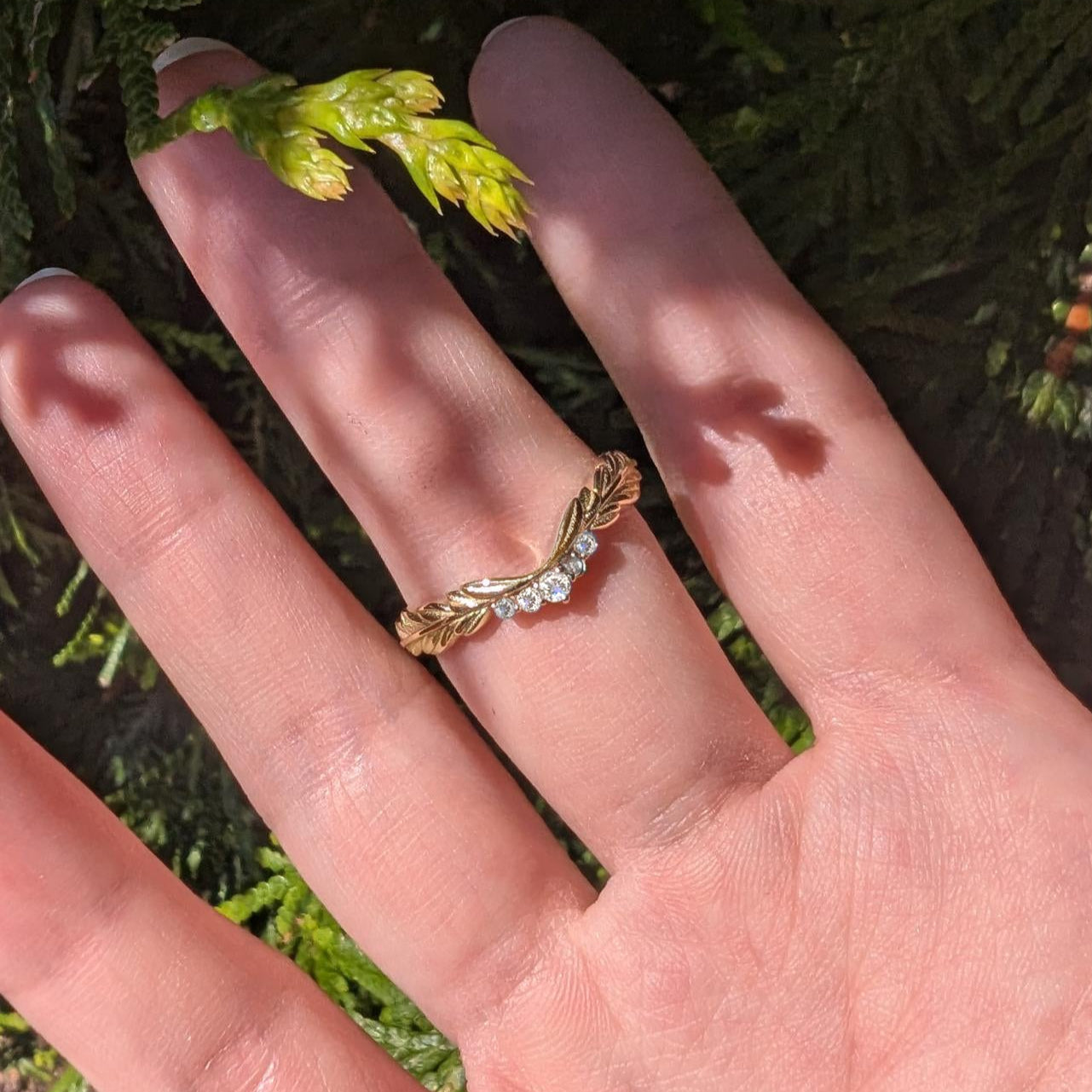 Gold ring with small diamonds on a person's finger against a natural background