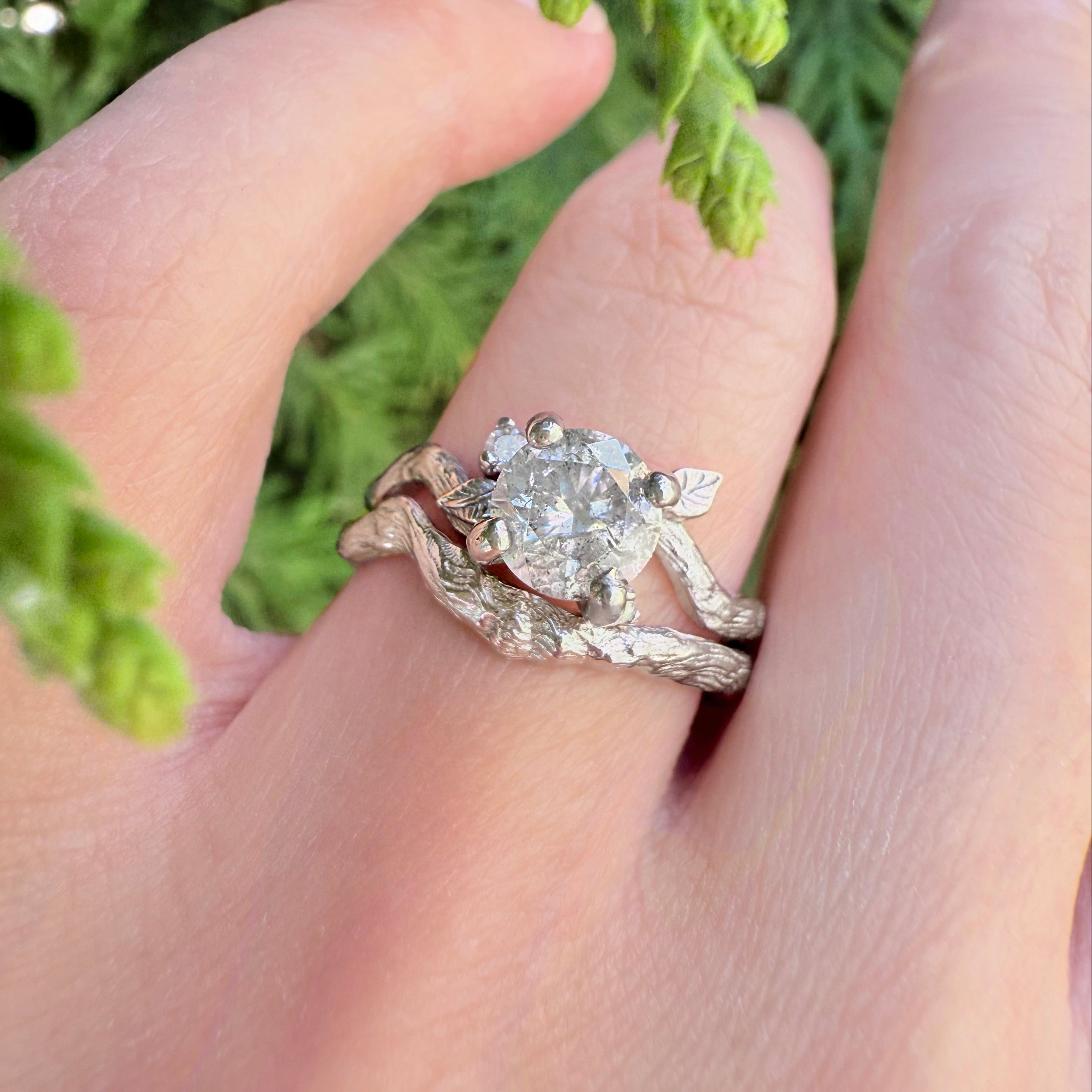 white gold ring with a diamond on a hand against a green leafy background
