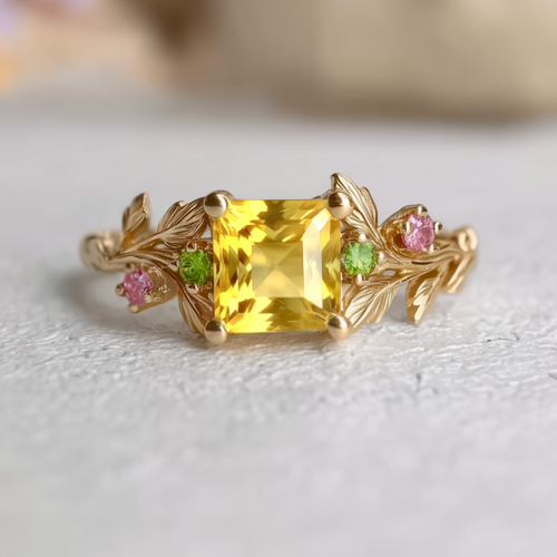 Gold ring with a yellow sapphire and pink and green gemstones on a light background