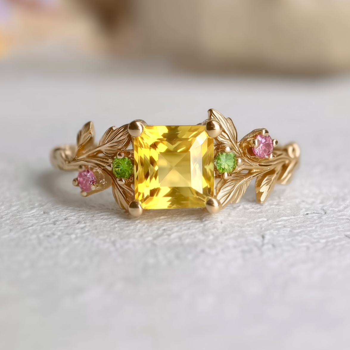 Gold ring with a yellow sapphire and pink and green gemstones on a light background